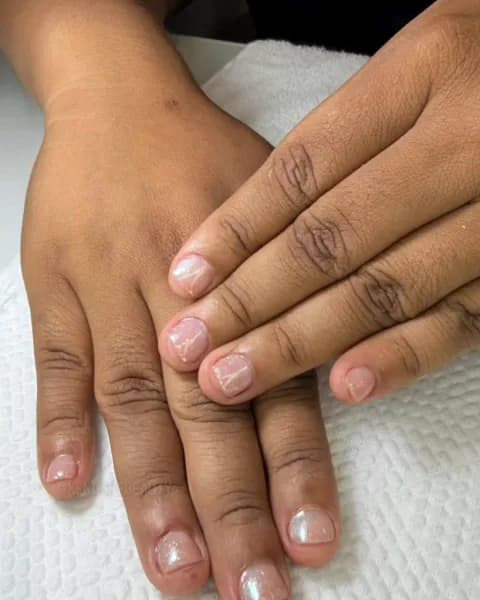 Mãos com unhas esmaltadas em tom claro sobre toalha branca